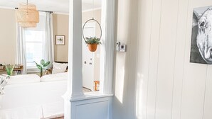 A room with a dining area featuring two chairs, a table with a black plate, and a vase of white flowers. There is a hanging plant and a painting on the wall. - Modern Farmhouse Suite at The Dorley (Sandusky)