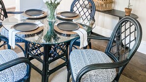 A dining area with a glass table surrounded by wicker chairs, a hanging plant, and a wall-mounted artwork. - Modern Farmhouse Suite at The Dorley (Sandusky)