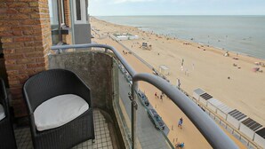 A balcony with a wicker chair, a view of a sandy beach with people and a calm sea. - Beautiful apartment in Oostende (Oostende)