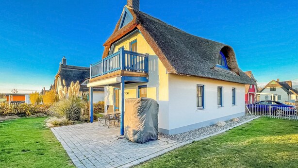 Ein traditionelles Haus mit Strohdach, einem Balkon und einer gepflasterten Terrasse.