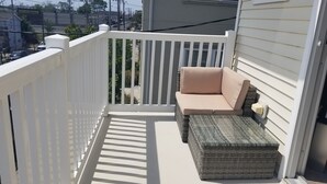 A balcony with a white railing, a beige sofa, and a wicker ottoman.