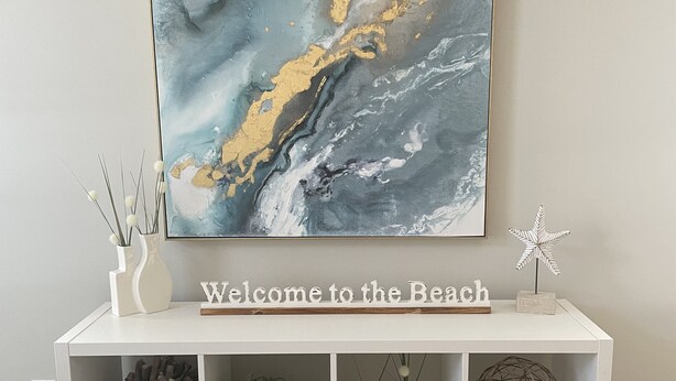 A white console table with a 'Welcome to the Beach' sign, decorated with plants, a starfish, and a spherical object.