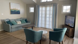 A living room with a grey sofa, teal armchairs, a coffee table, and a TV on a wooden stand.