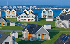 Zona residencial costera con casas modernas que tienen balcones, paneles solares y un puerto deportivo al fondo.