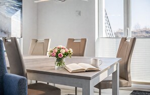 A dining table with chairs, a vase of flowers, an open book, and a coffee cup.