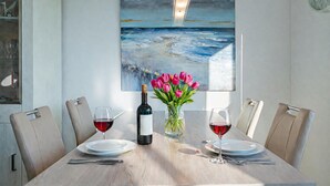 Una mesa de comedor con dos copas de vino, una botella y un jarrón con tulipanes rosados.