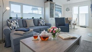 Una sala de estar moderna con un sofá gris, una mesa de centro con una tetera, un florero y una estantería.