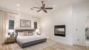 Un dormitorio moderno con una cama grande, ventilador de techo, chimenea y vistas al exterior.