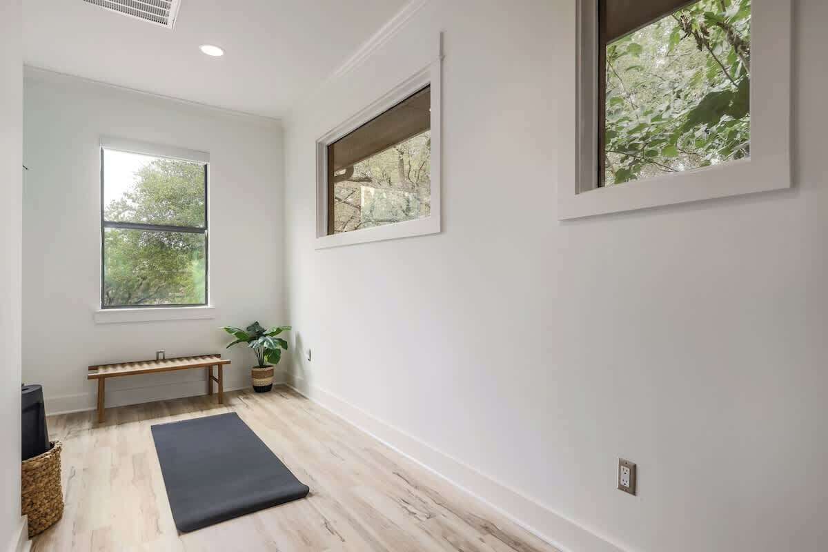 Um quarto com um banco de madeira, um tapete de exercício preto e um vaso com planta.