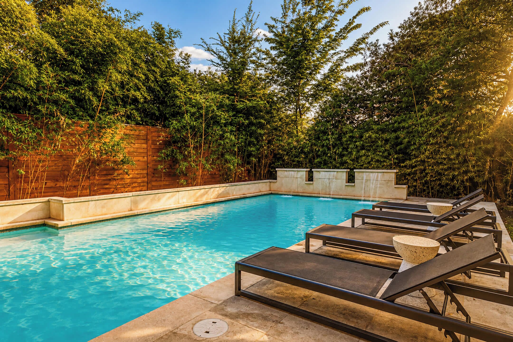 Une piscine entourée d’une clôture en bois, avec des arbres en arrière-plan.