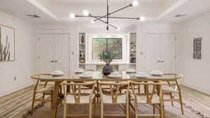 Un comedor con una mesa redonda, sillas de madera, una araña y paredes blancas.