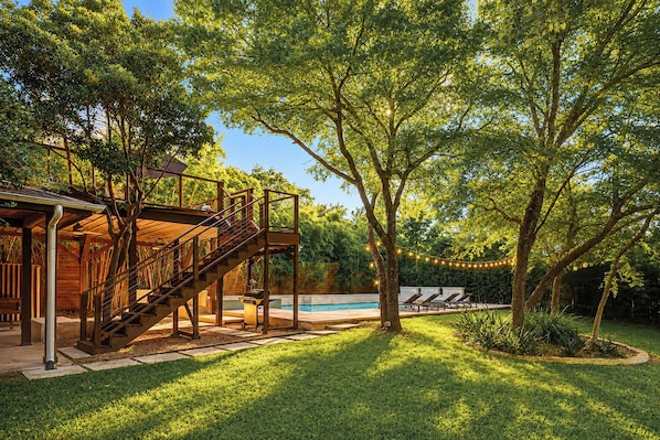 A wooden deck with a staircase leading to a covered area, a swimming pool, and a well-maintained lawn.