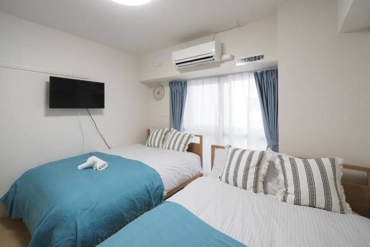 A hotel room with two beds, a flat-screen TV, an air conditioning unit, and a clock on the wall.
