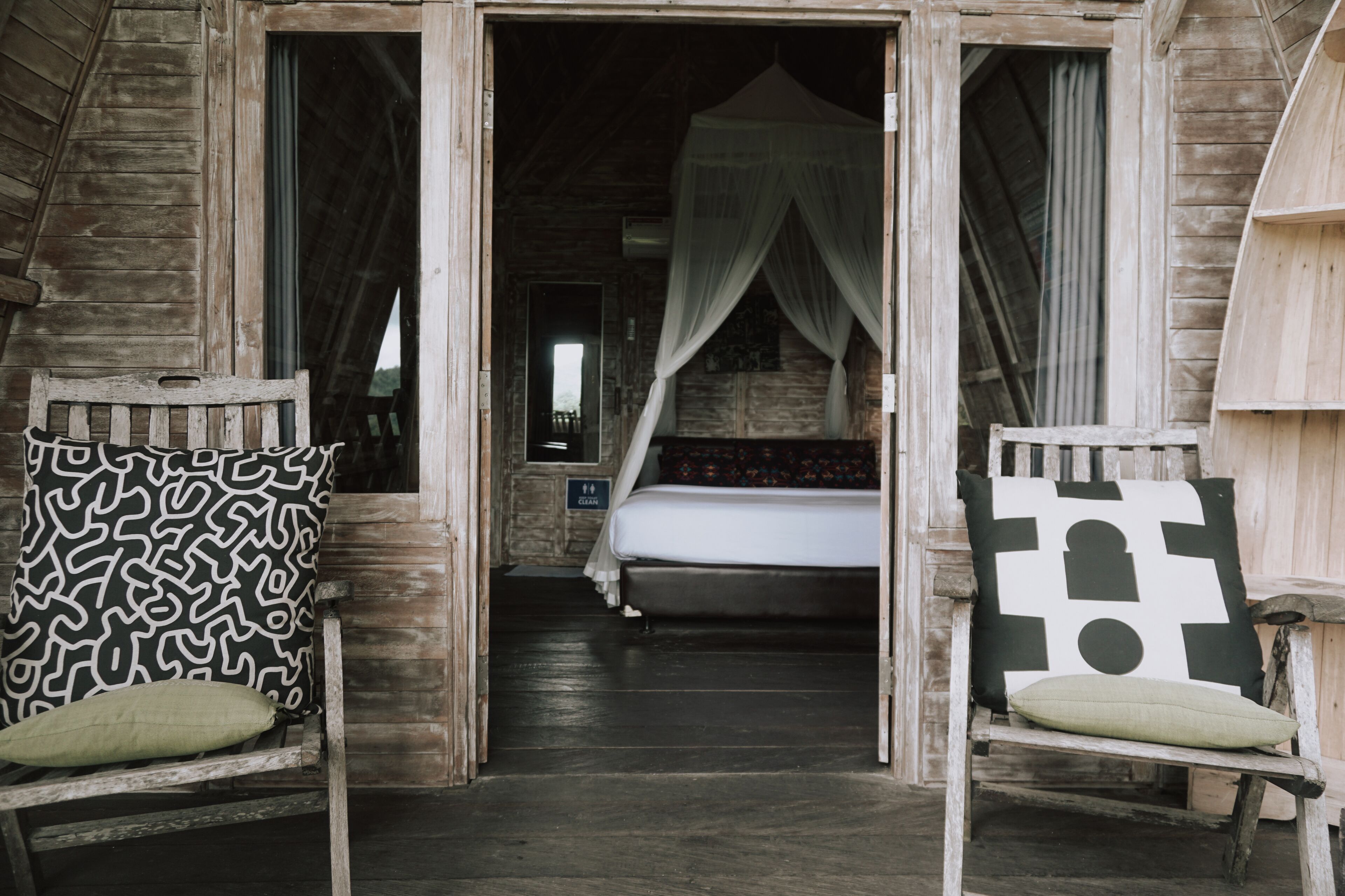 A wooden room with a bed, a chair, and a bench. There is a canopy over the bed.