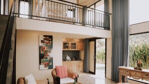 A spacious living area with a high ceiling, a balcony, a kitchen, and a view of greenery. - Natural View Sidemen Cottage (Sidemen)