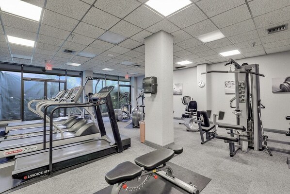 Une salle de sport équipée de tapis de course, d’appareils de musculation et d’un banc.