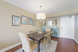 A dining room with a wooden table, beige chairs, a chandelier, framed artwork, and a blue cabinet.