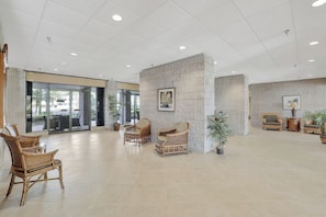 A spacious lobby with wicker chairs, a central column with a framed picture, and potted plants.