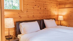 A wooden cabin room with a bed, two bedside lamps, and a window. - Izu House Luxury Log with Cozy Fireplace (Ito)