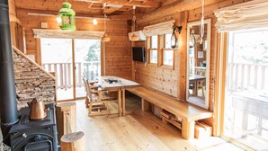 A wooden cabin with a stone fireplace, wooden dining table, benches, and large windows. - Izu House Luxury Log with Cozy Fireplace (Ito)