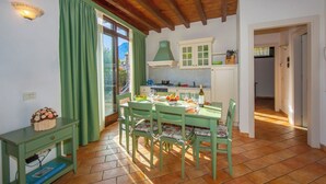 Comedor con mesa dispuesta para cuatro, una silla verde, una mesita con una cesta y una ventana con cortinas.