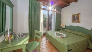 Una habitación con una cama, una mesa con una botella y vasos, una silla y una ventana con cortinas.