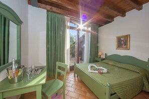 A room with a bed, a table with a bottle and glasses, a chair, and a window with curtains.
