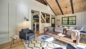 A spacious living room with a high ceiling, a large window, a built-in staircase, and a cozy seating area. - Sleek Cabin w/ Deck, 8 Miles to Mount Snow & Hikes (Wilmington)