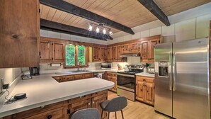 A modern kitchen with wooden cabinets, a stainless steel refrigerator, and a large island with bar stools. - Sleek Cabin w/ Deck, 8 Miles to Mount Snow & Hikes (Wilmington)