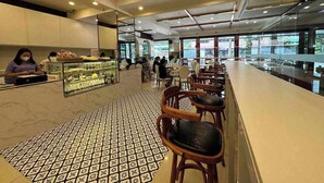 A spacious cafe with a tiled floor, wooden chairs, and a counter with a display case. - Northpointe Residences (Quezon City)
