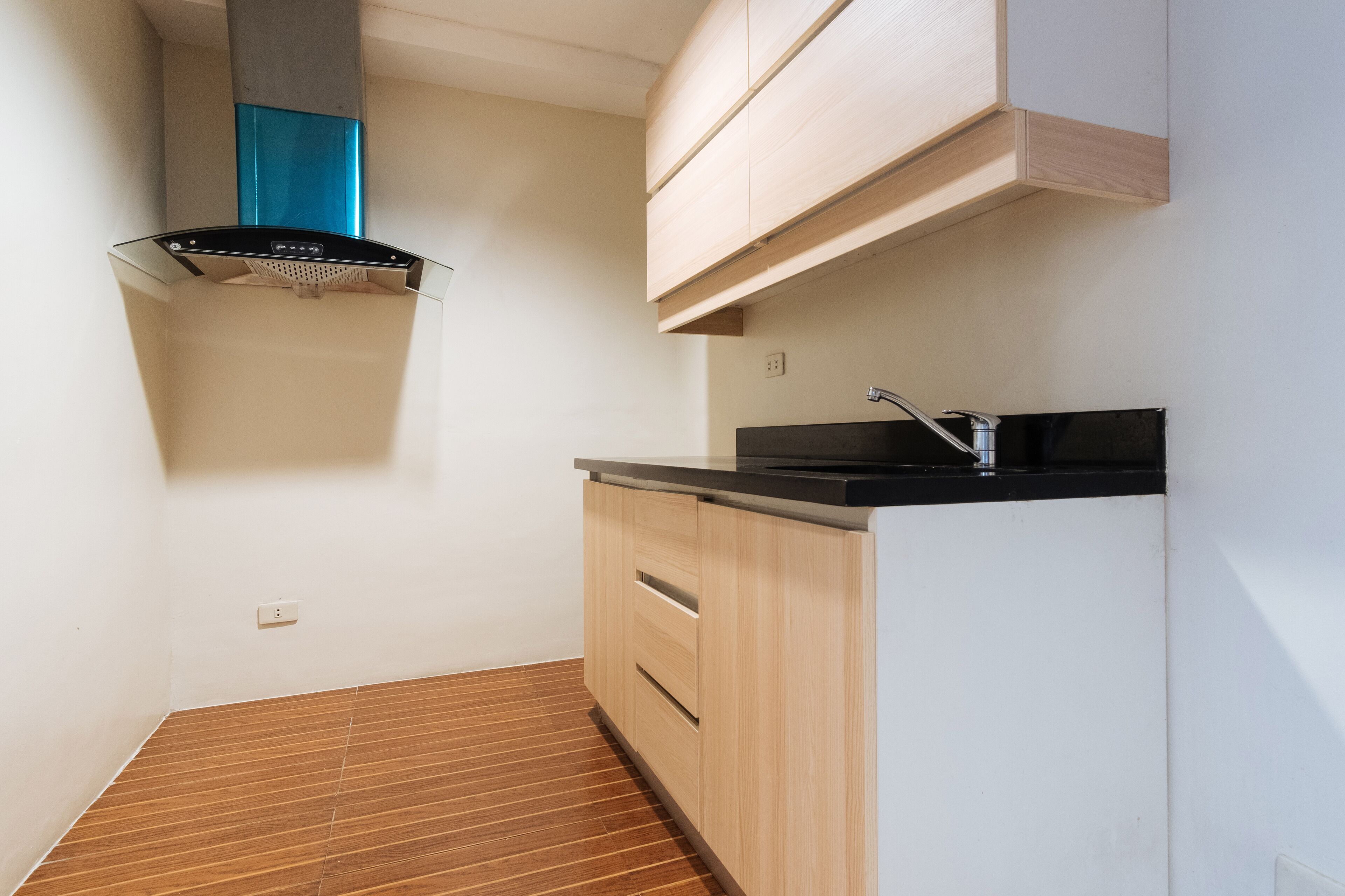 A compact kitchen with a black countertop, wooden cabinets, and a stainless steel sink.