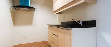 A compact kitchen with a black countertop, wooden cabinets, and a stainless steel sink.