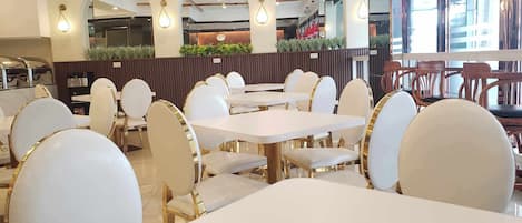A restaurant interior with white tables and chairs, arched windows, and pendant lighting.