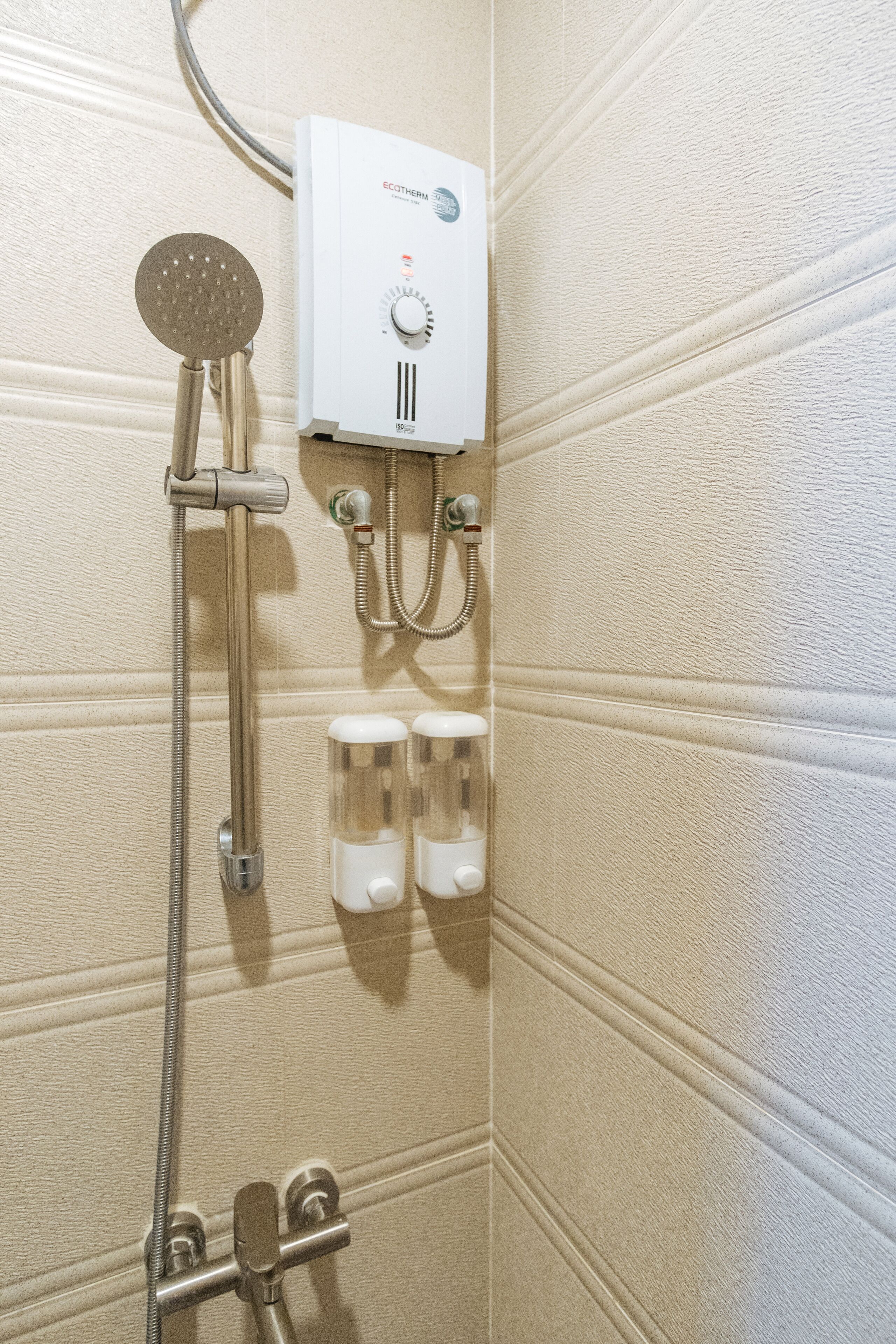 A bathroom with a wall-mounted shower, a control panel, and two soap dispensers.