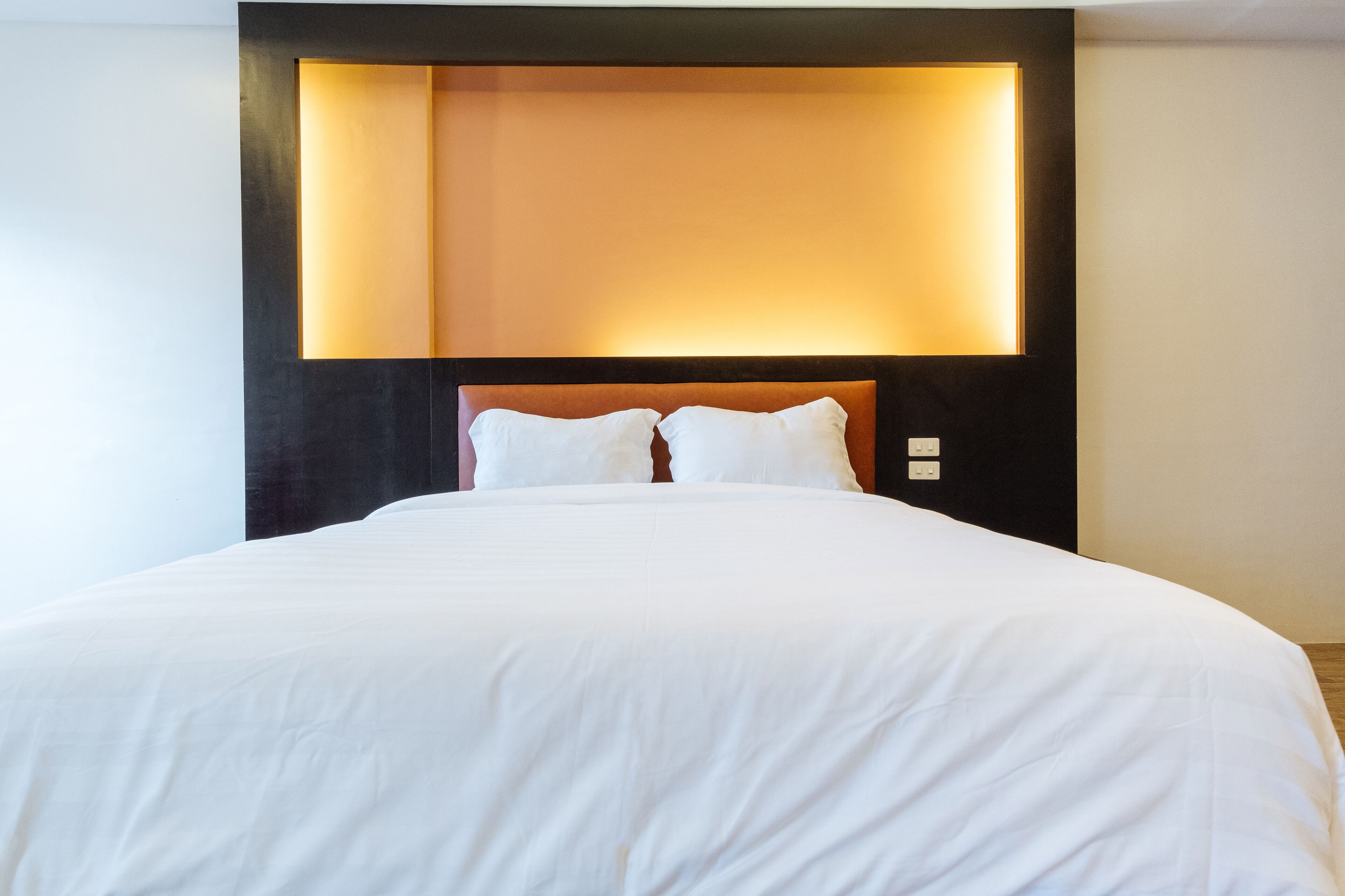 Een net opgemaakt bed met witte lakens en een hoofdbord met geïntegreerde verlichting.