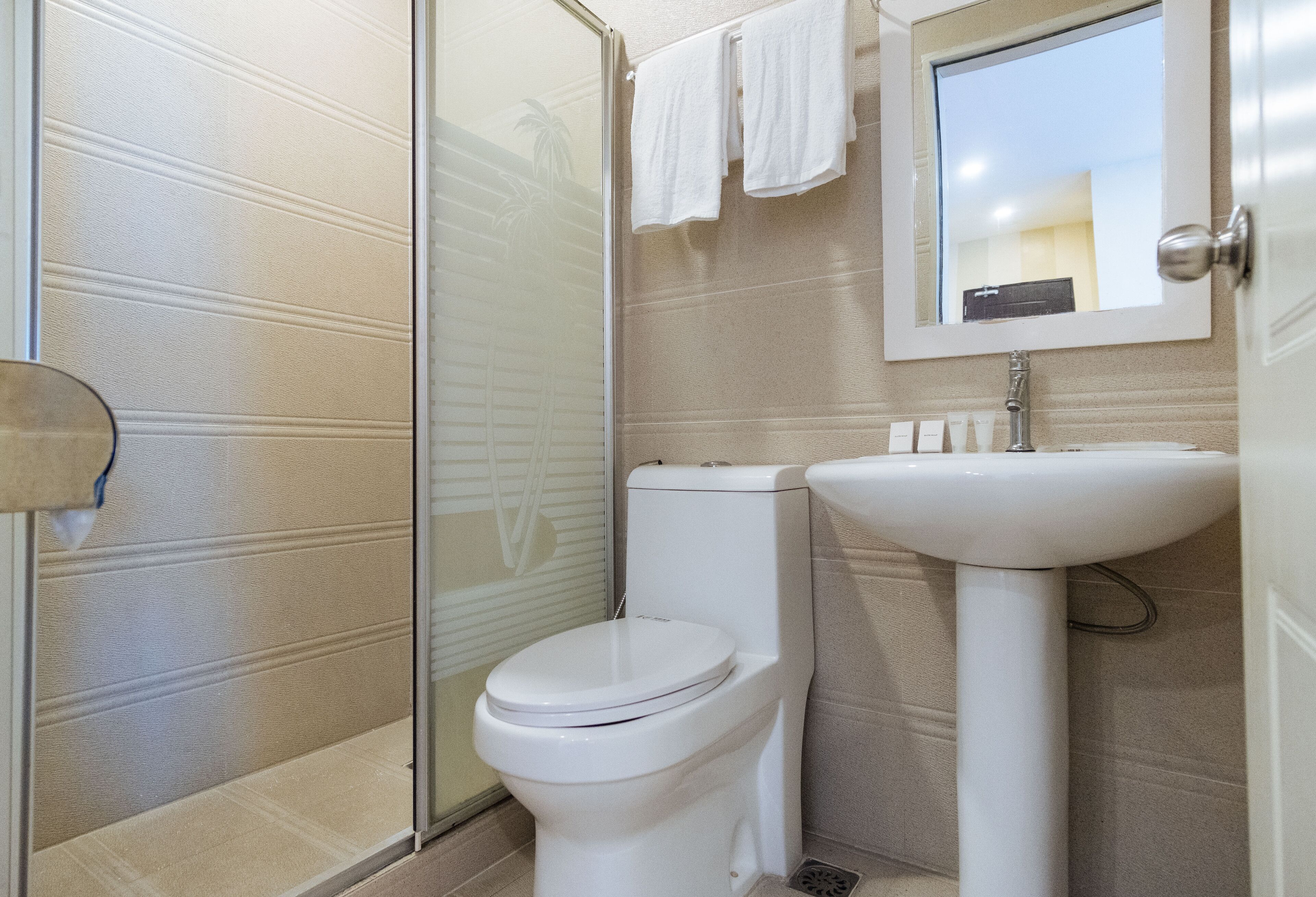Un baño con cabina de ducha de vidrio, un inodoro blanco y un lavamanos pedestal.