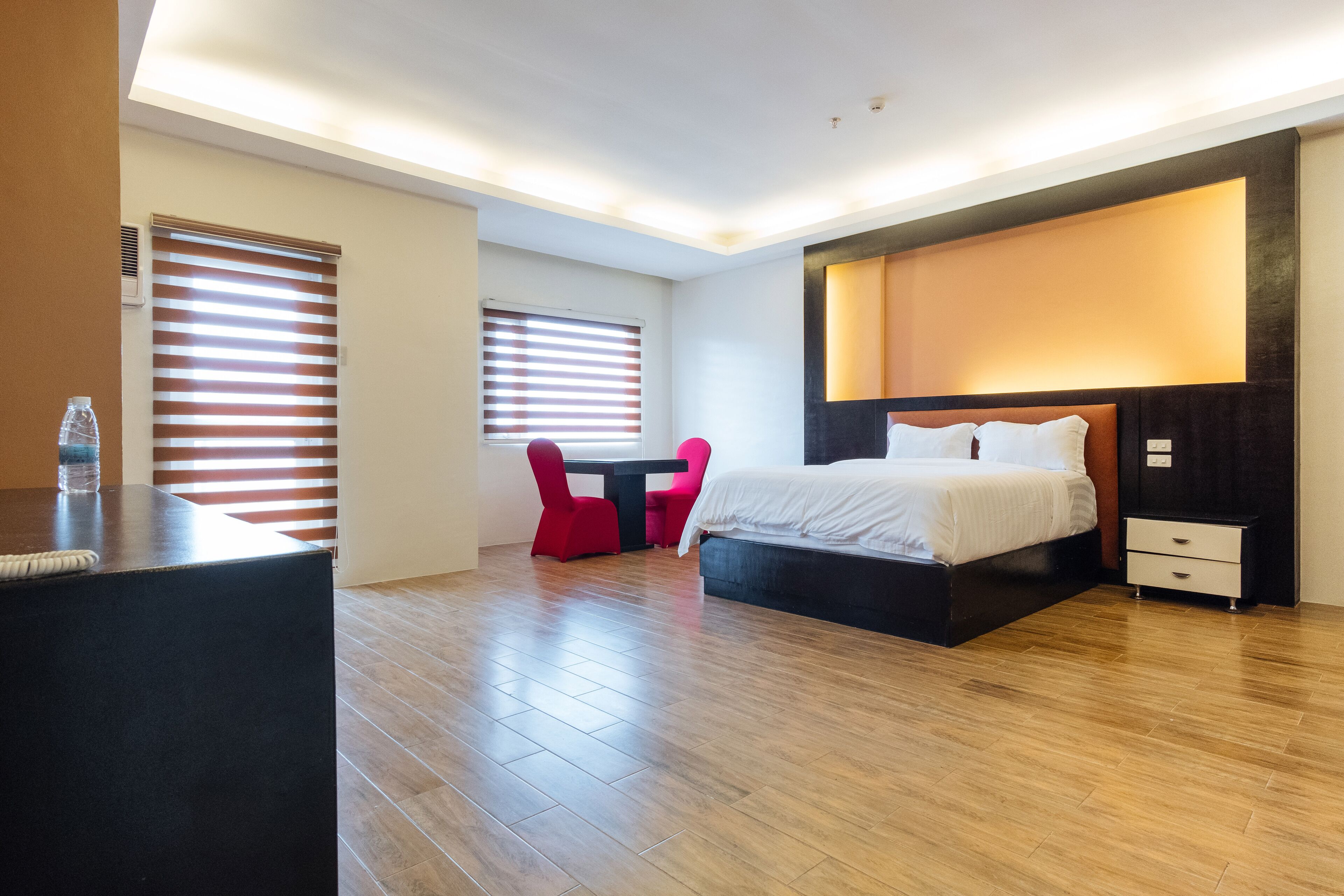 Moderni hotellihuone, jossa on suuri sänky, yöpöydät, työpöytä tuolilla sekä ikkuna, jossa on sälekaihtimet.