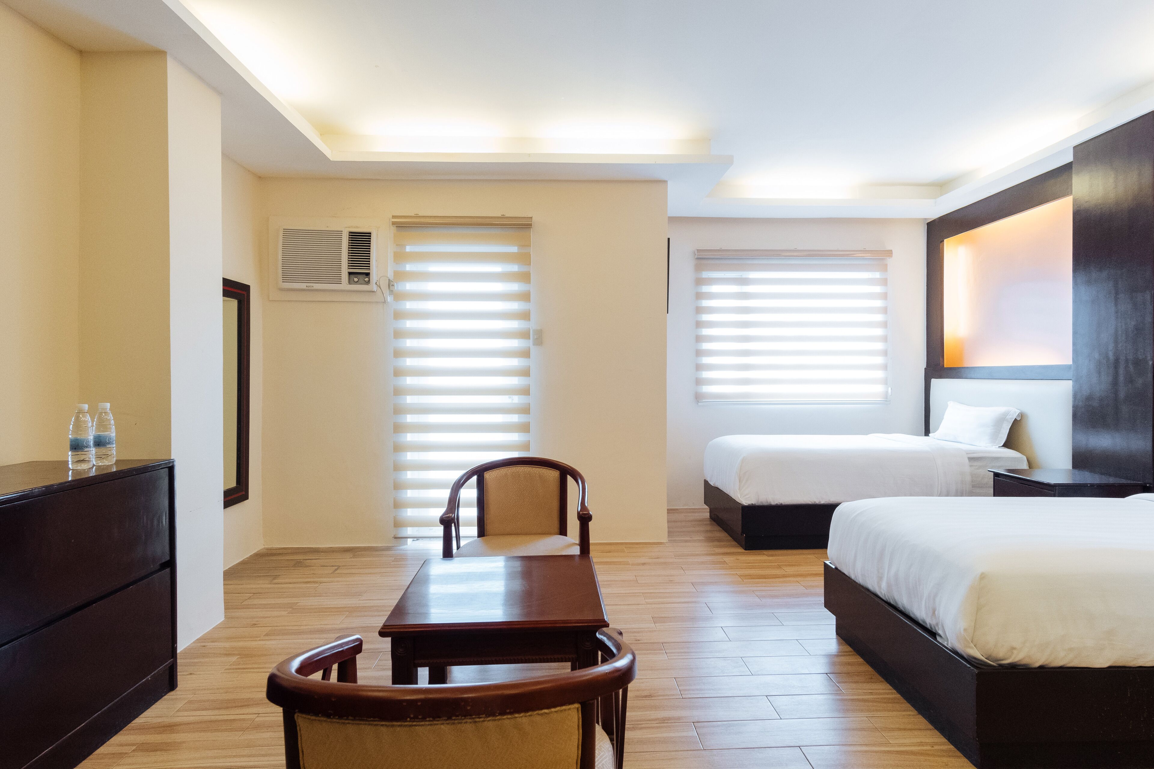 A hotel room with a wooden floor, a desk with two chairs, a bed, and a dresser.