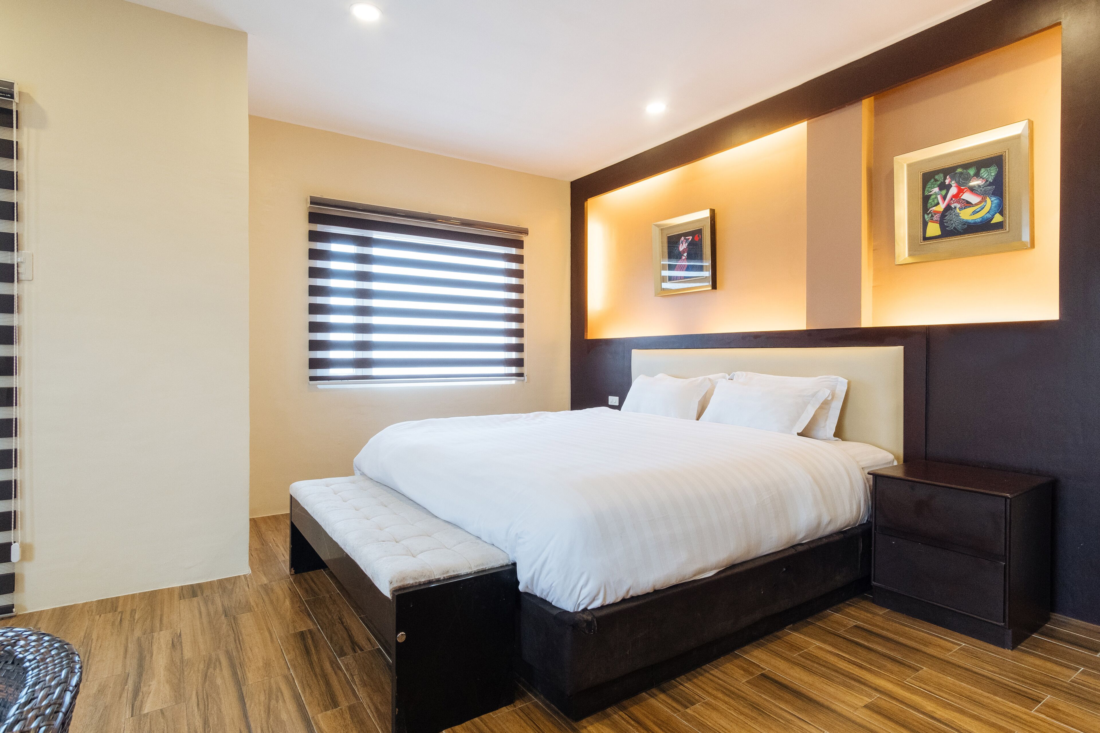 A modern bedroom with a large bed, a bench, a nightstand, and a window with blinds.