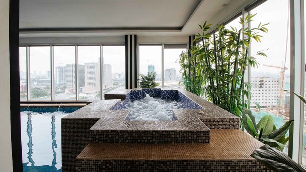 A modern indoor hot tub with a city view, surrounded by large windows and indoor plants. - Northpointe Residences (Quezon City)