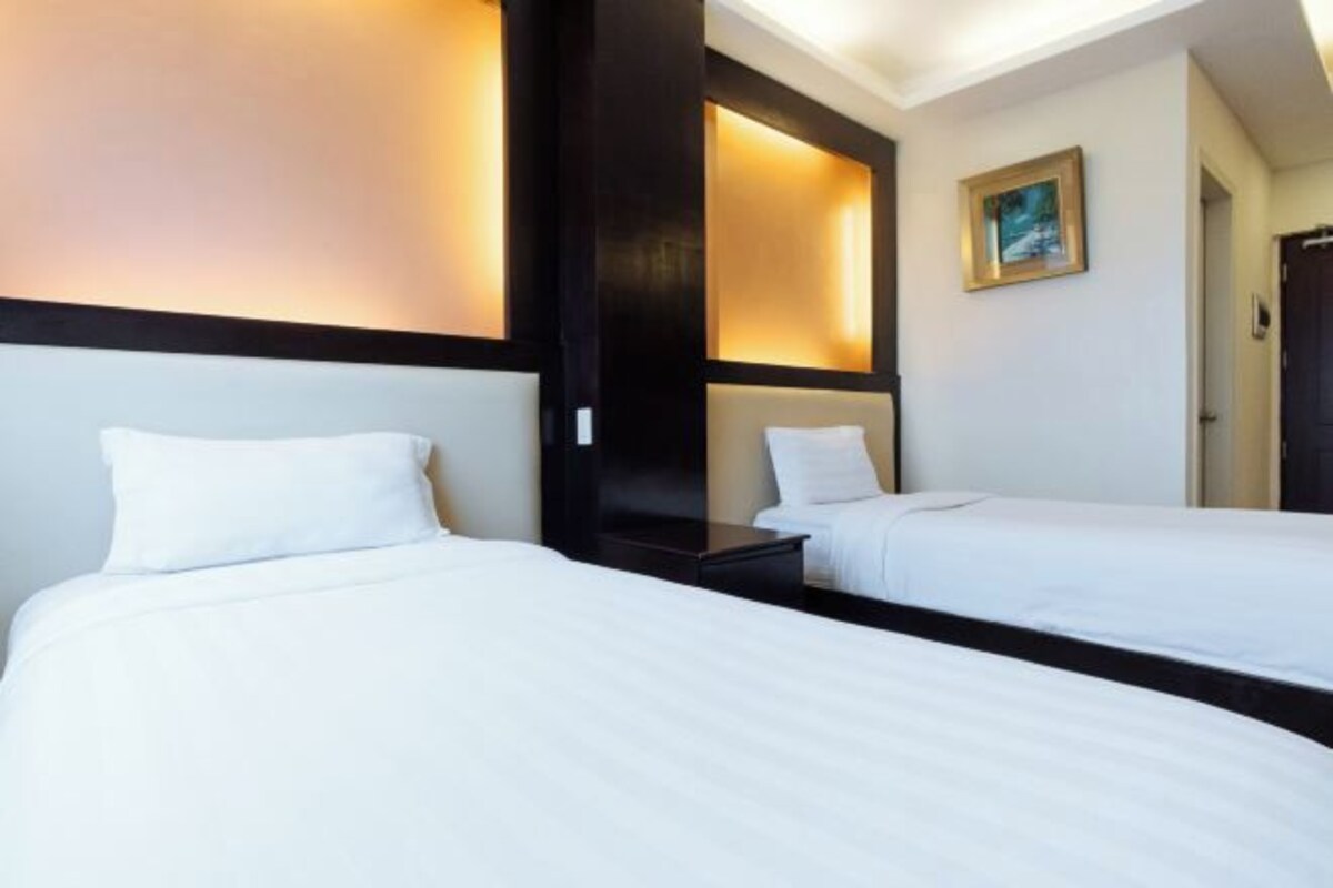 A hotel room with two single beds, a nightstand, a wall-mounted shelf, and a framed picture.