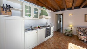 Une cuisine avec des meubles blancs, une cuisinière à gaz et un évier. Le plafond est en bois et un des murs est peint en vert.