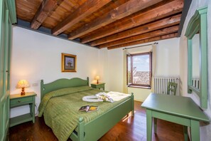 A room with a wooden ceiling, a bed with a green headboard, a bedside table with a lamp, a window with a view, and a green chair.