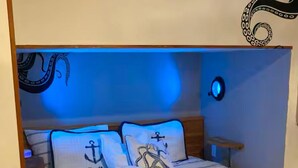 Un lit avec une couvre-lit à motifs nautiques, deux oreillers ornés d’ancres et un luminaire fixé au mur.