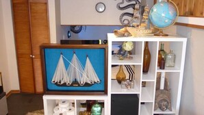 Une pièce comprenant une armoire en bois, une œuvre d’art encadrée représentant des voiliers, un globe terrestre et divers objets décoratifs disposés sur des étagères.