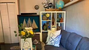 Un salon chaleureux avec un canapé gris, une table d’appoint en bois sur laquelle sont posés un globe terrestre et des objets décoratifs, et un tapis moelleux.