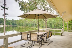 Relax on the deck overlooking the serene water, surrounded by lush trees and a comfortable seating area.