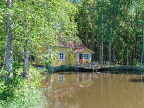 A yellow cabin with a red roof, surrounded by trees and a calm body of water. - Piispasen torppa by Interhome (Loimaa)