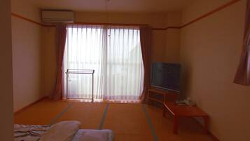 A hotel room with a bed, a television on a stand, and a sliding glass door with curtains.
