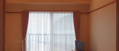 A hotel room with two beds, a television, a small table, and a window with curtains.